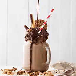 Iced chocolate drink decorated with cream, nuts, wafers and cookies, topped with chocolate syrup