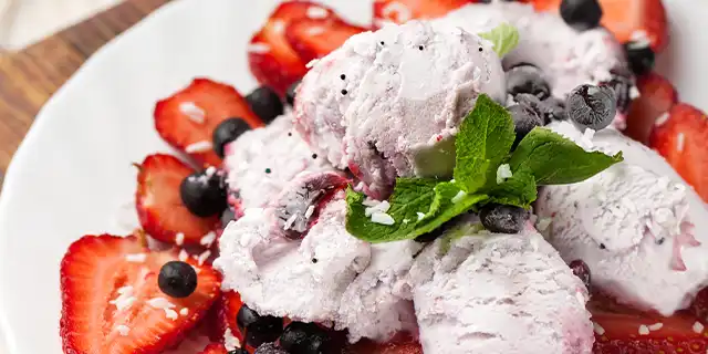 A bowl with 2 visible scoops of ice creamed, dotted with flecks of black pepper and garnished with fresh sliced strawberries