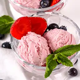 A bowl with two scoops of mixed berry ice cream, garnished with slice strawberries an, blueberries, and mint