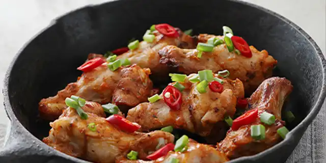 A plate of sauced chicken drumlets with some vegetables and garnished with chillies