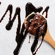 Chocolate syrup poured over a spoon to showcase its sleek finish