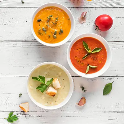 Three different types of sauces inside small white bowls garnished with various leaves