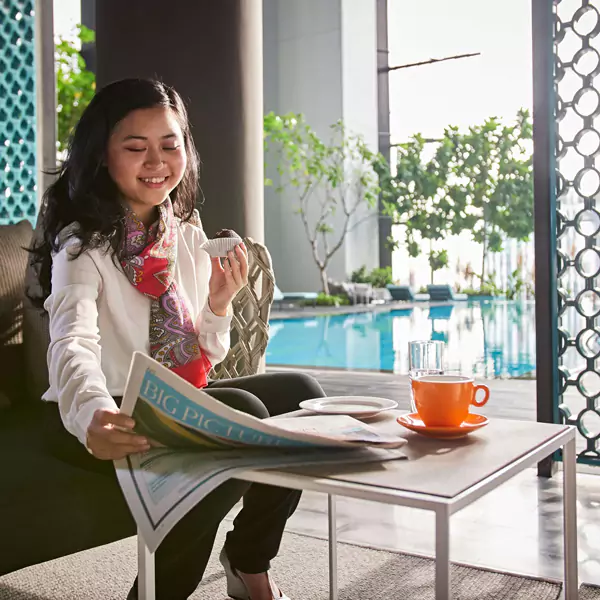 Woman sitting on the couch and reading a newspaper whilst eating chocolate muffin