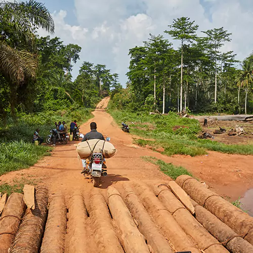 Man on a scooter that has a brown burlap bag attached to it on a rural road