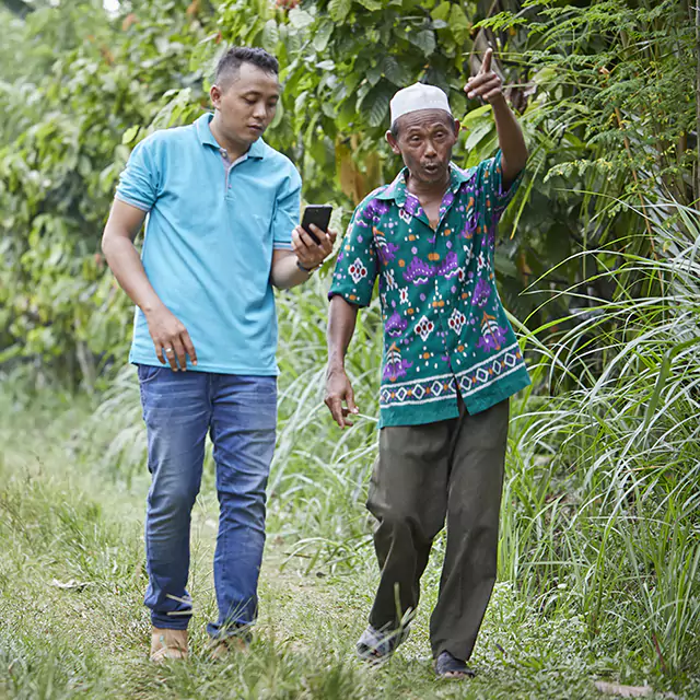 One men holding a cellphone whist walking a another man in a forest